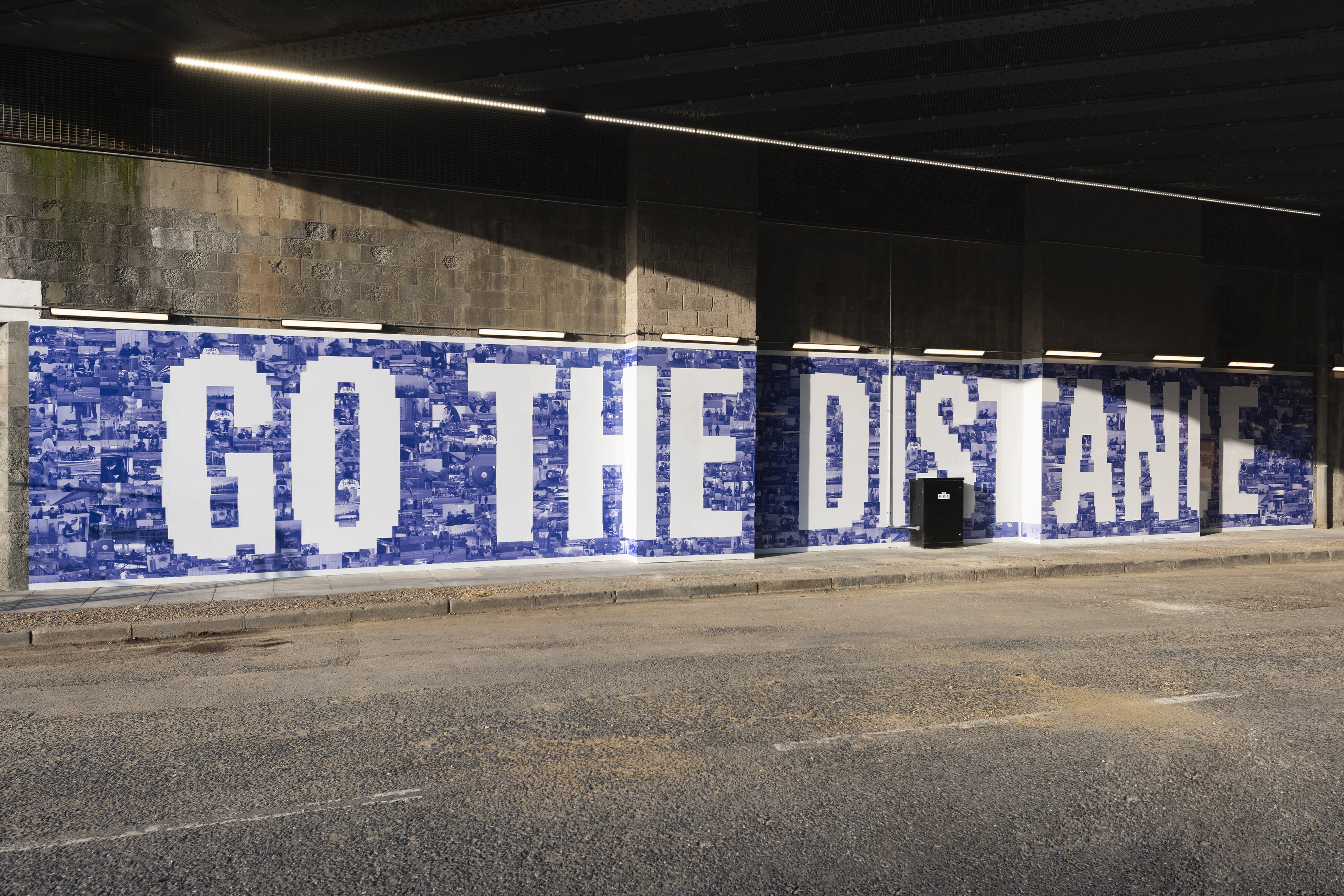 A wide artwork made up of blue photographs with the words "Go the Distance" in white lettering, on a concrete wall.