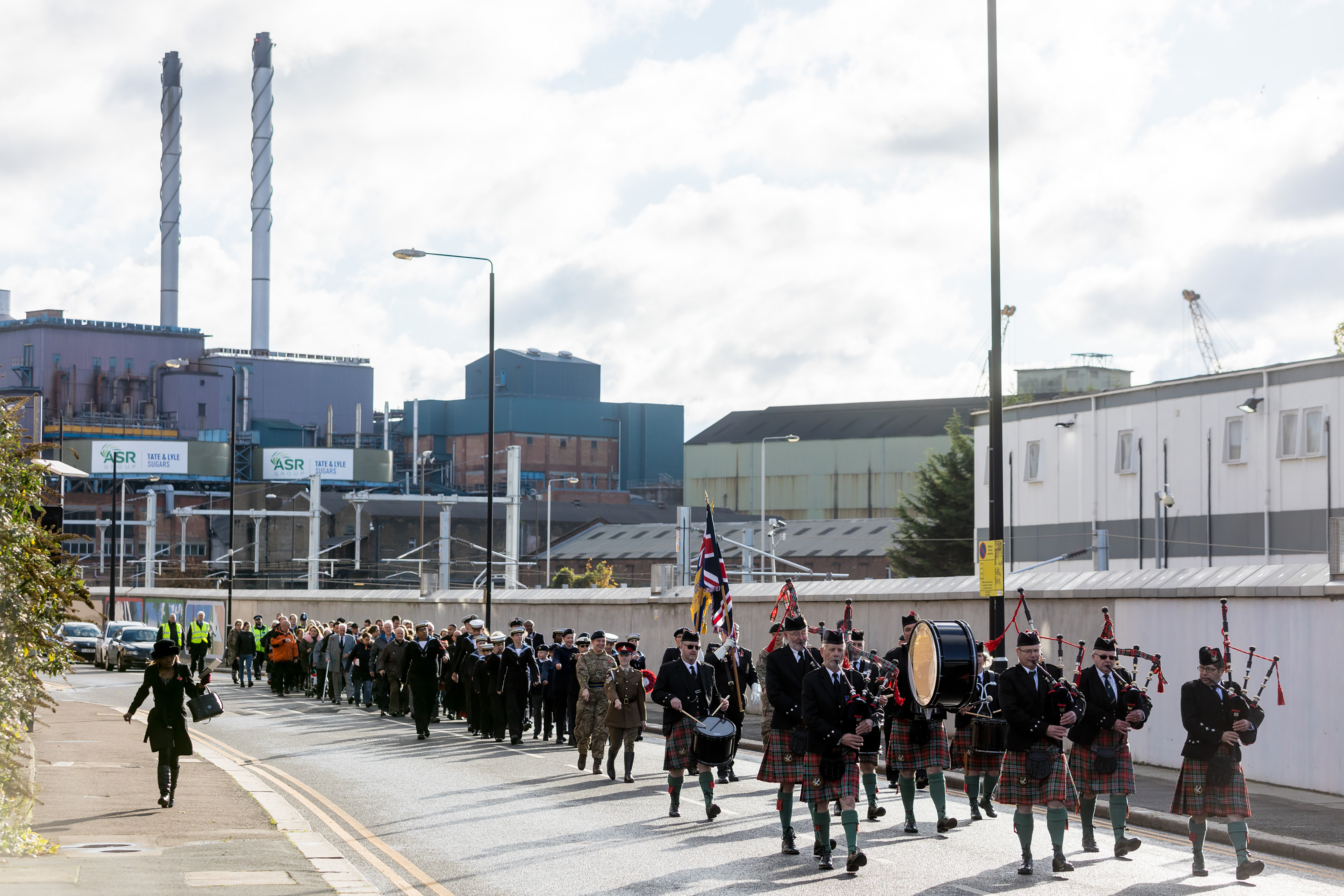 A photograph of a large group of bag pipe players and soldiers parading in front of a trackside wall.