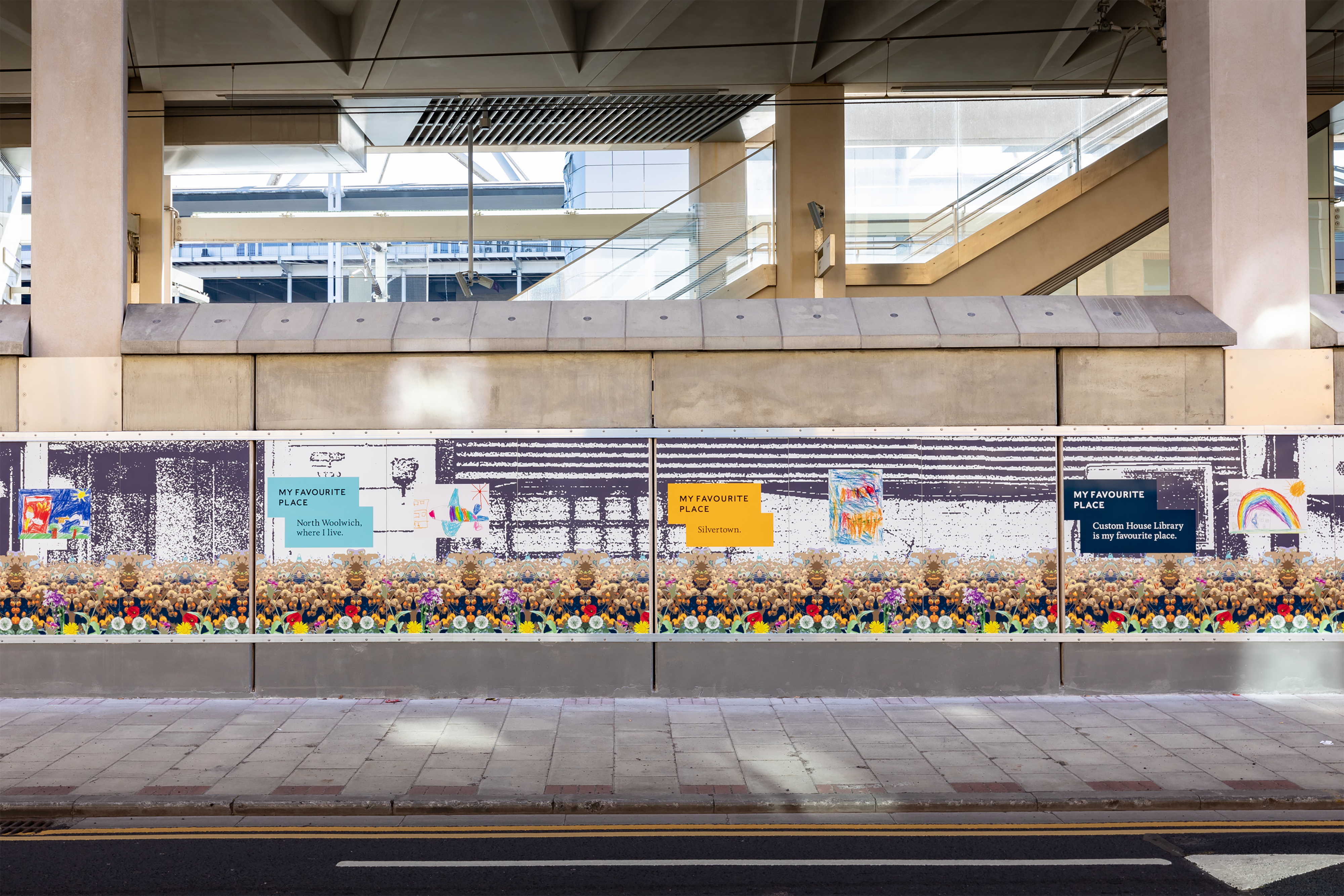 A photograph of a colourful trackside wall displaying children's drawings on a street.