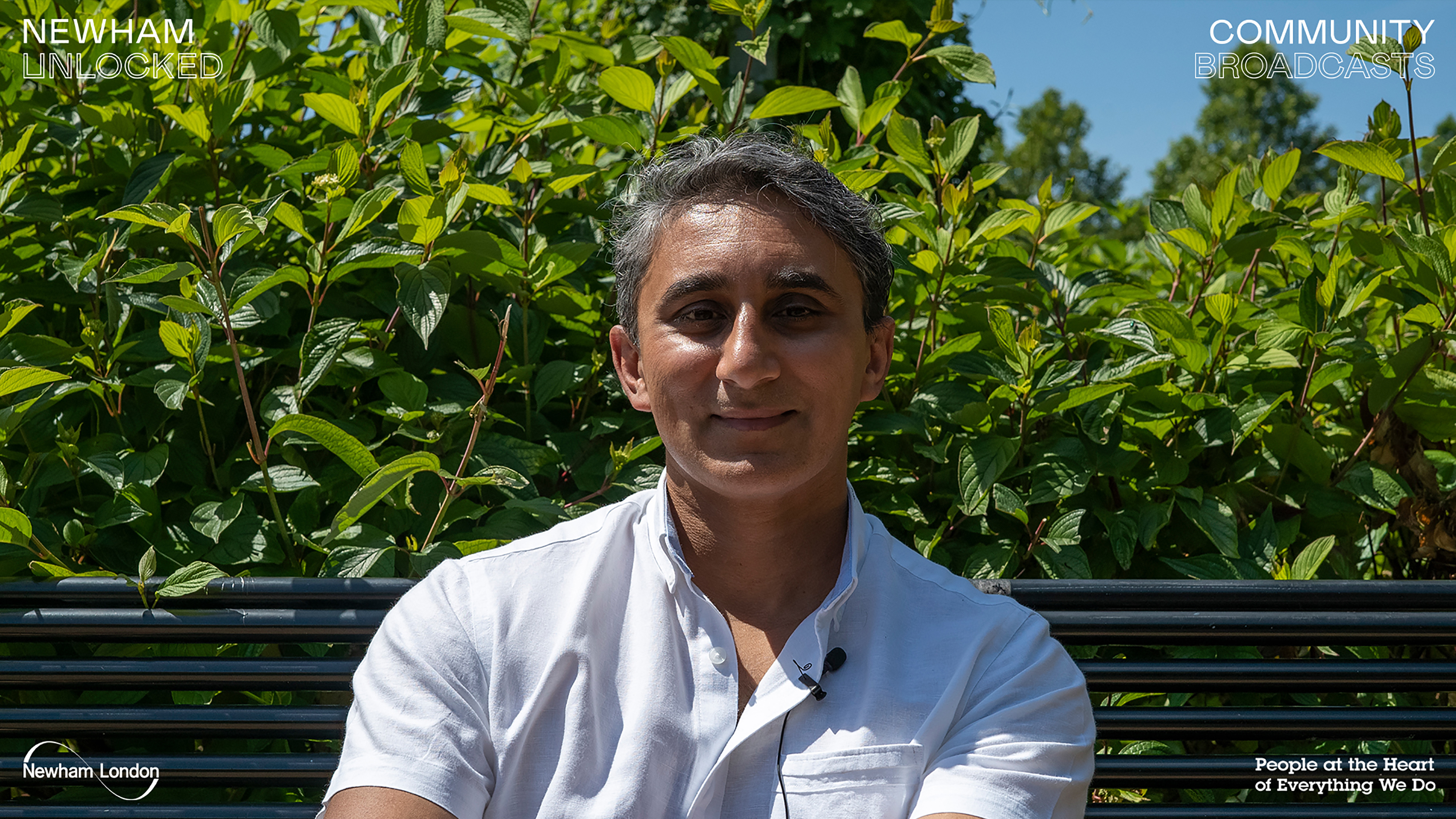 A photograph of a South Asian man sitting on a park bench.
