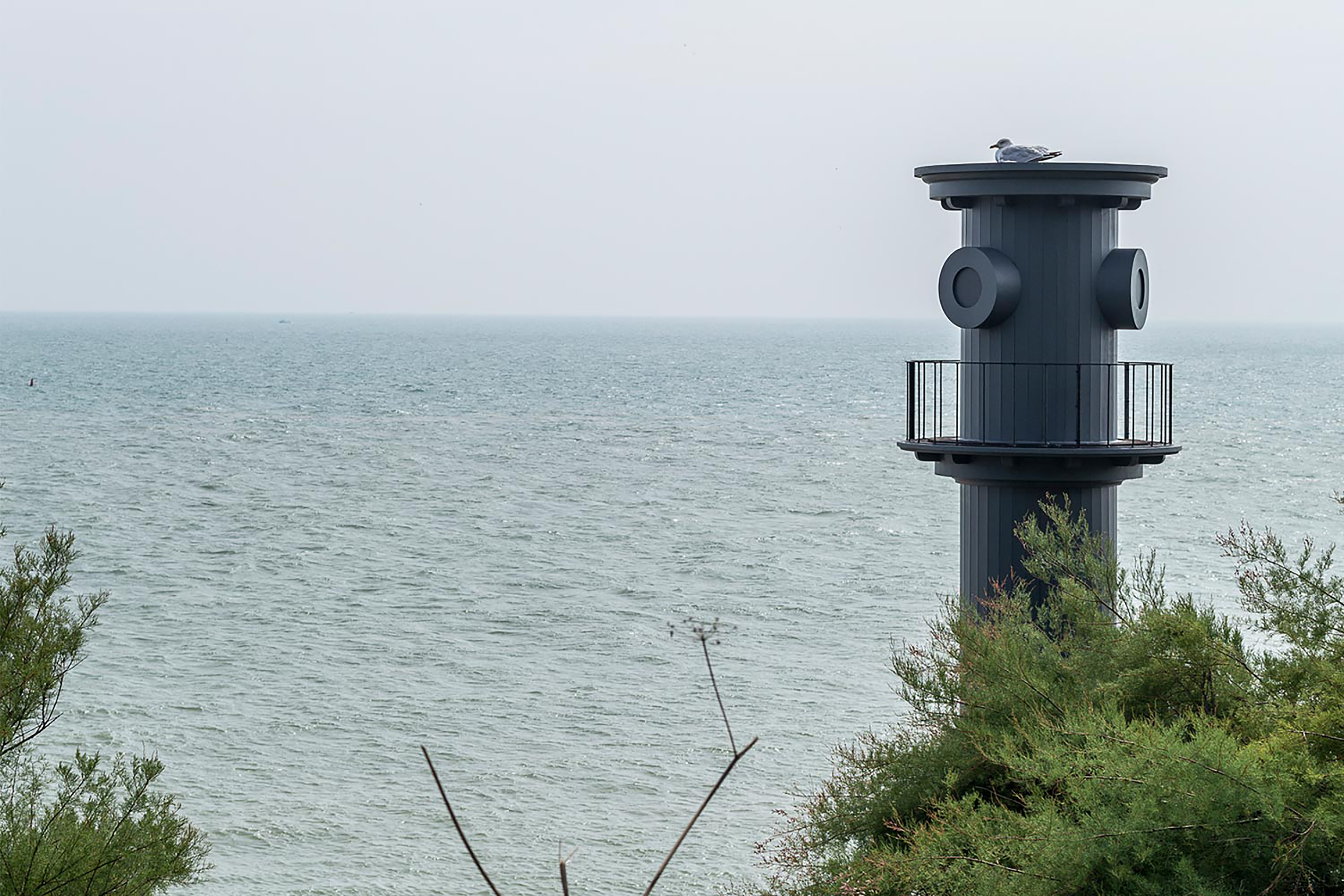 A photograph from the coastline onlooking the sea and a beach hut structure built in the architectural style of Hawksmoor.