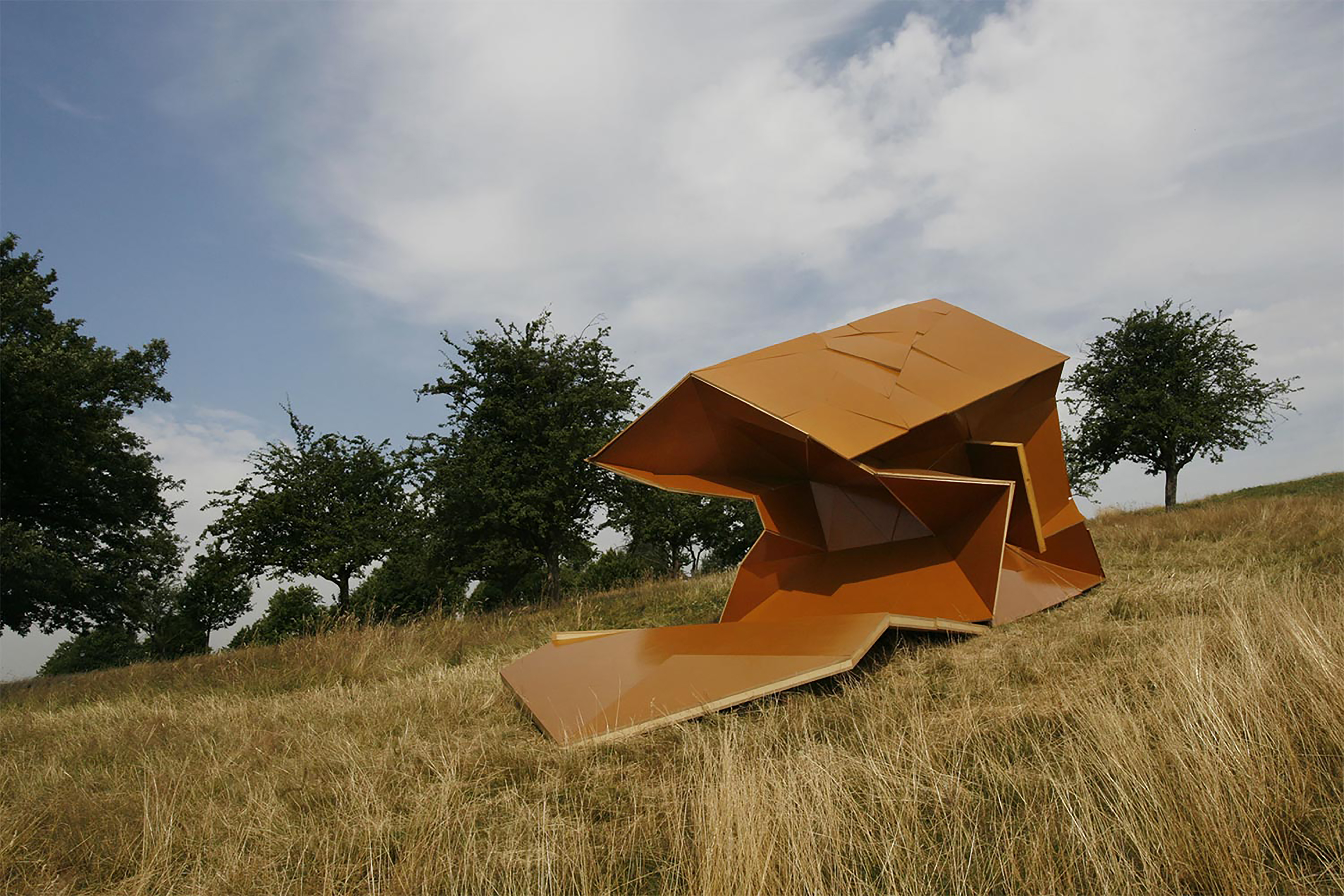 A large brown sculpture made up of geometric shapes in a wheat field.