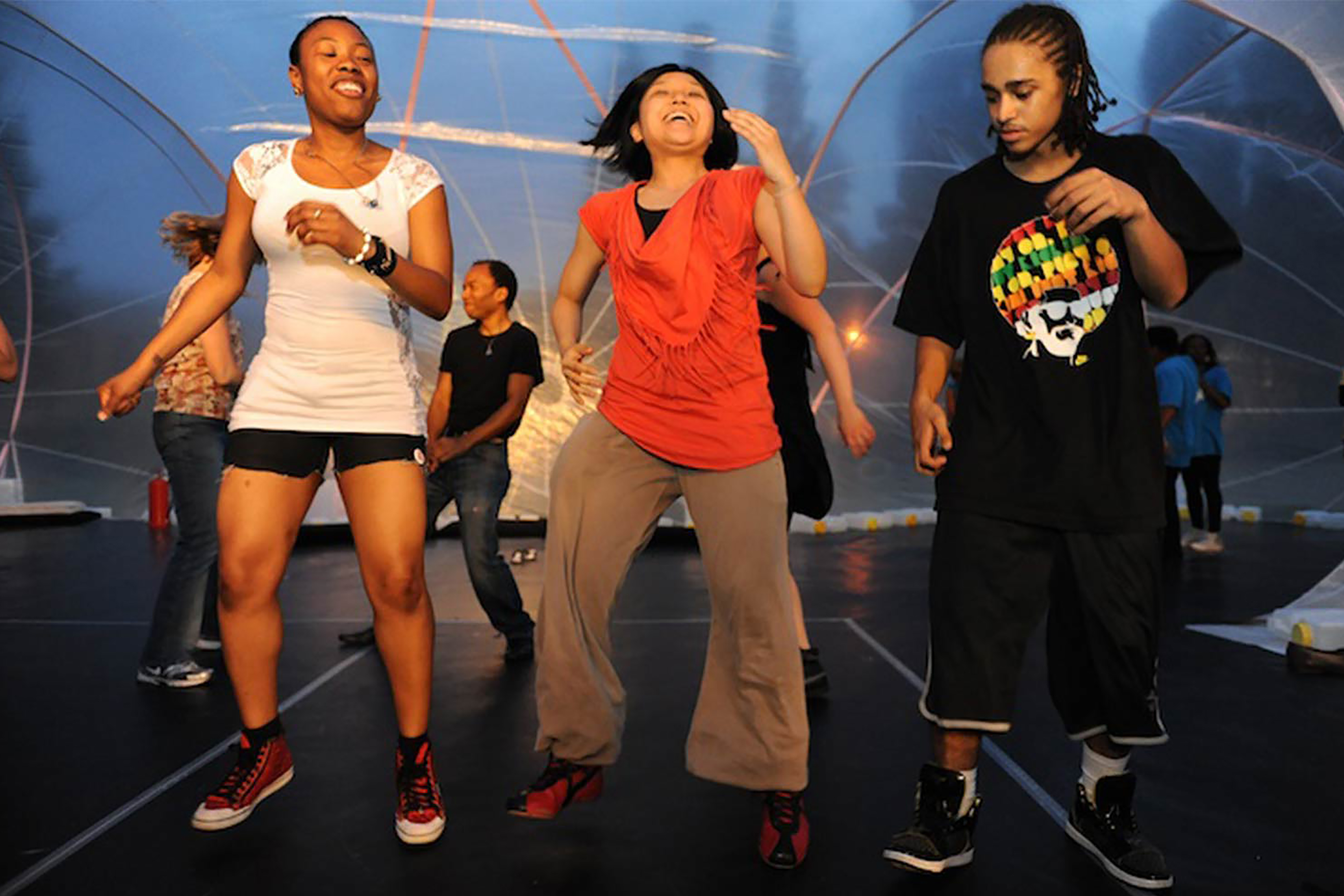 A photograph of a group of women dancing inside a transparent tent at night.