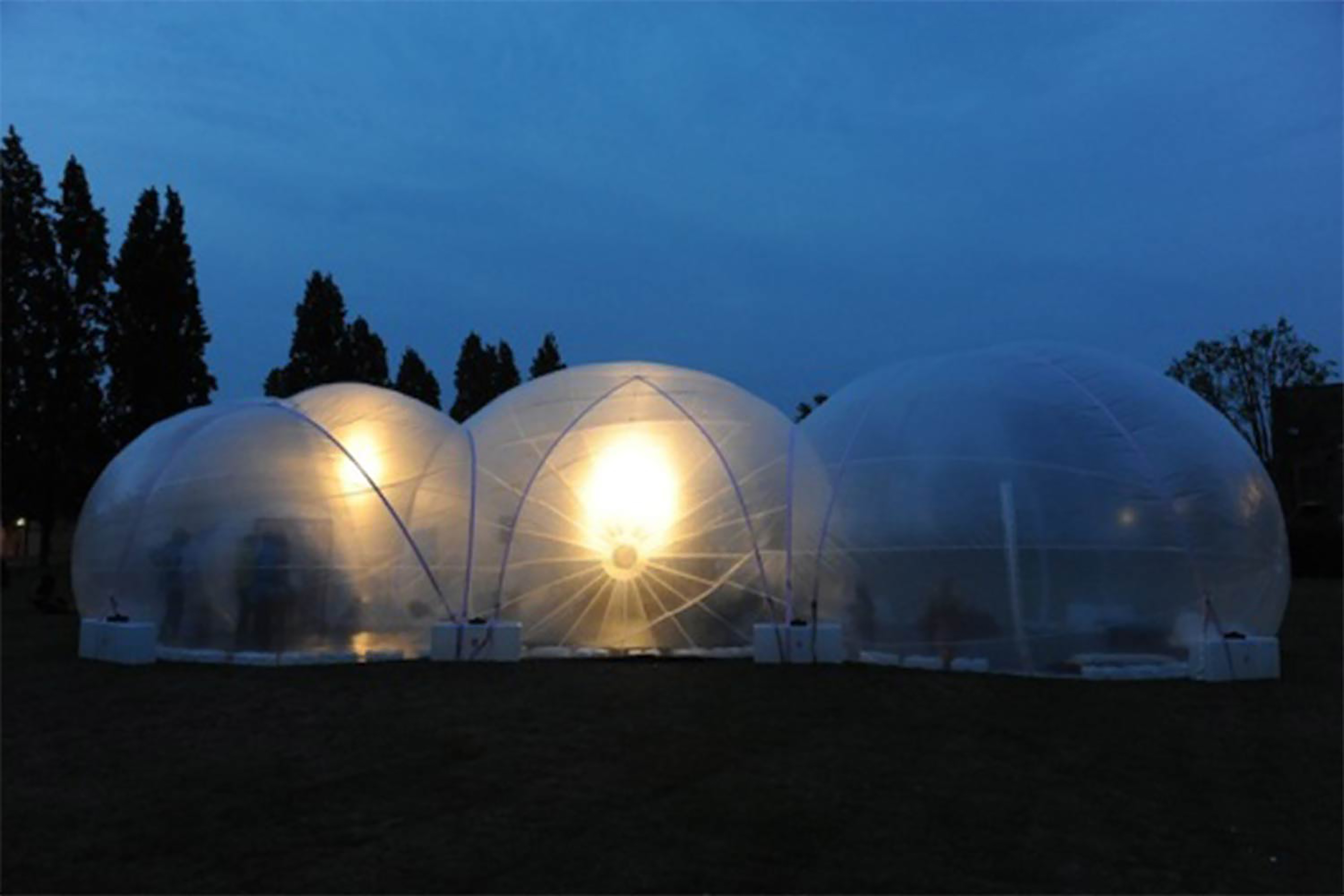 A large see-through plastic inflatable bubble-like structure in a large grass field at night.