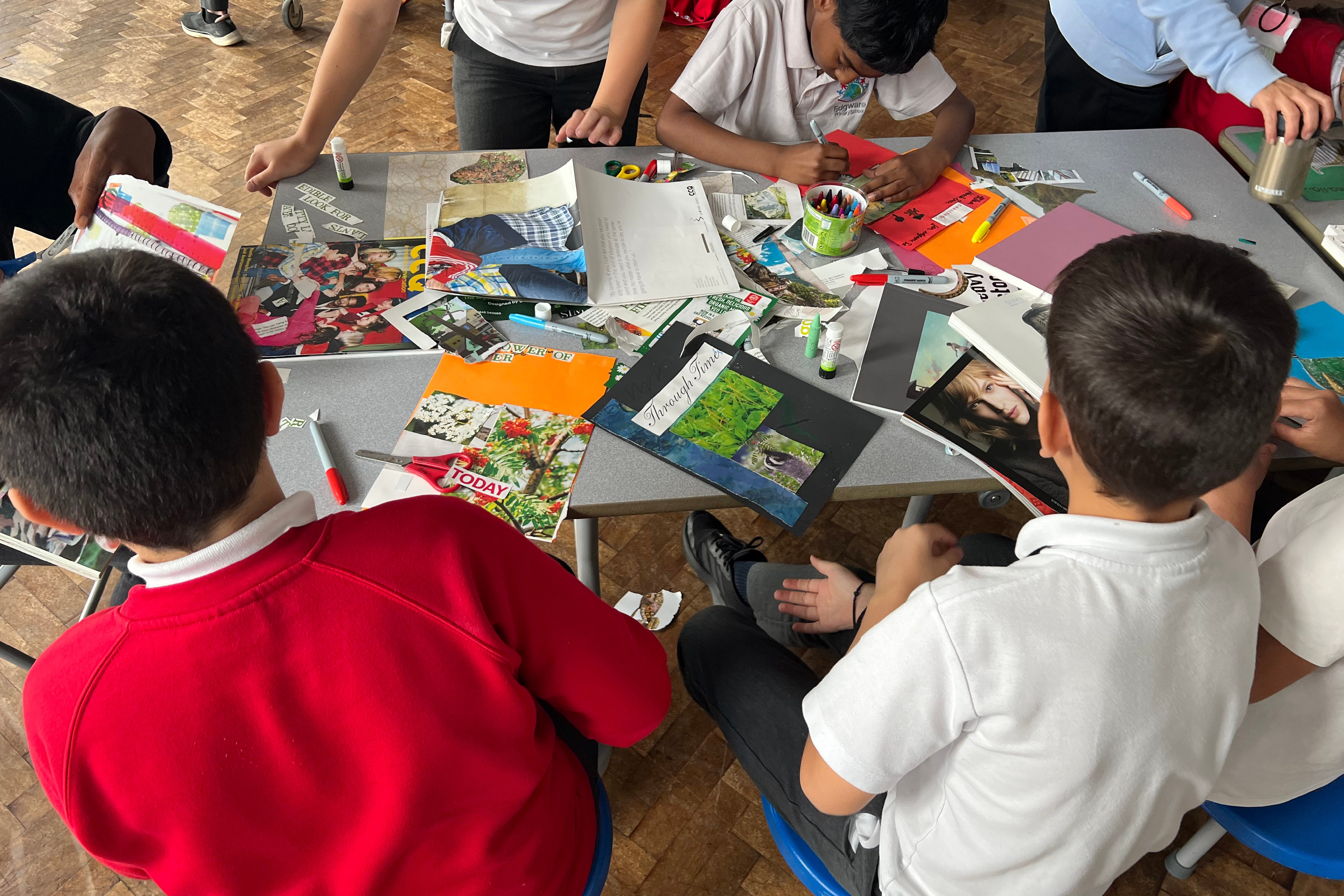 A group of school children around a table cutting out images and texts from various magazines to make posters on colourful pictures.