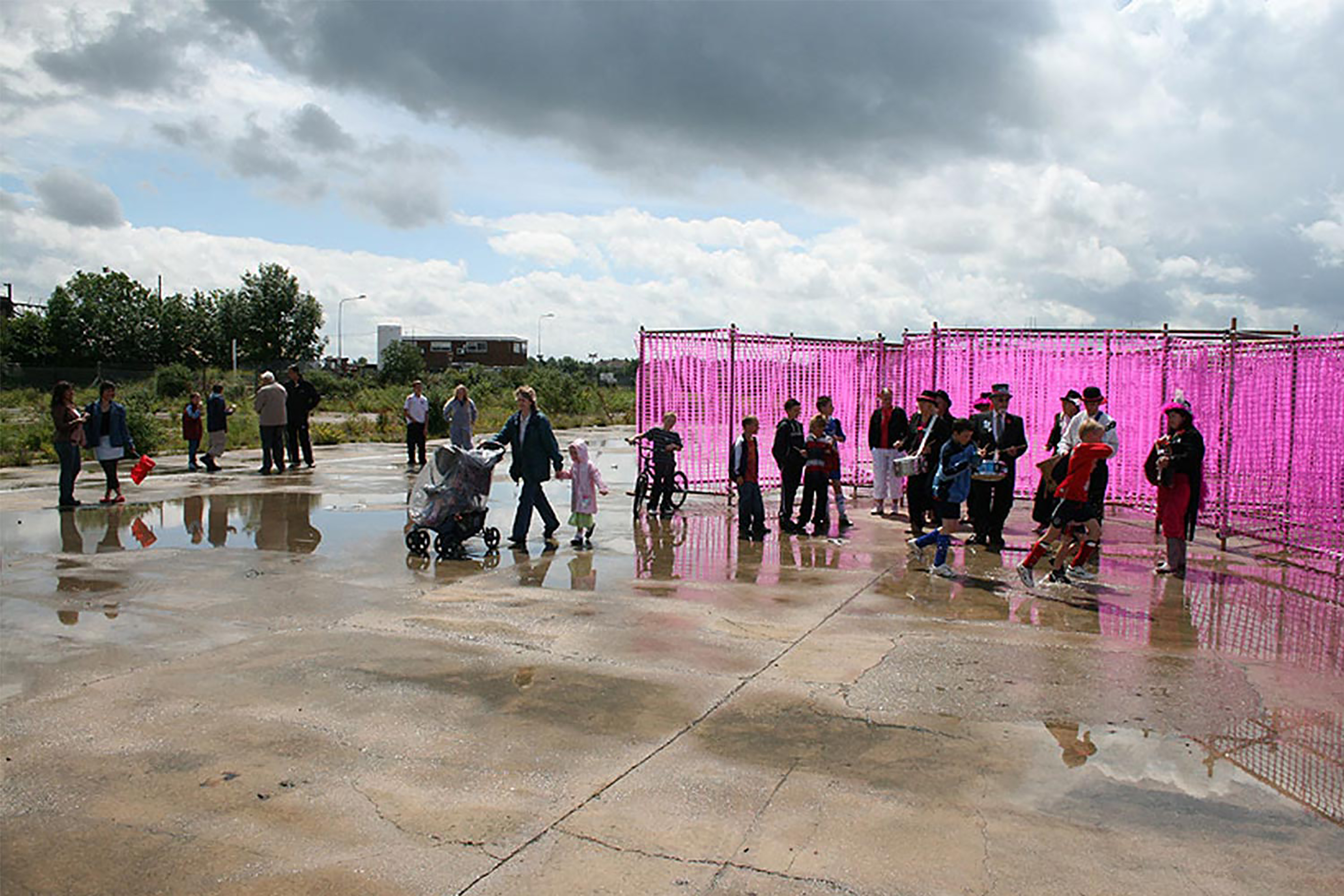 A photograph of a group of adults and children loitering outside a maze constructed of pink tape.