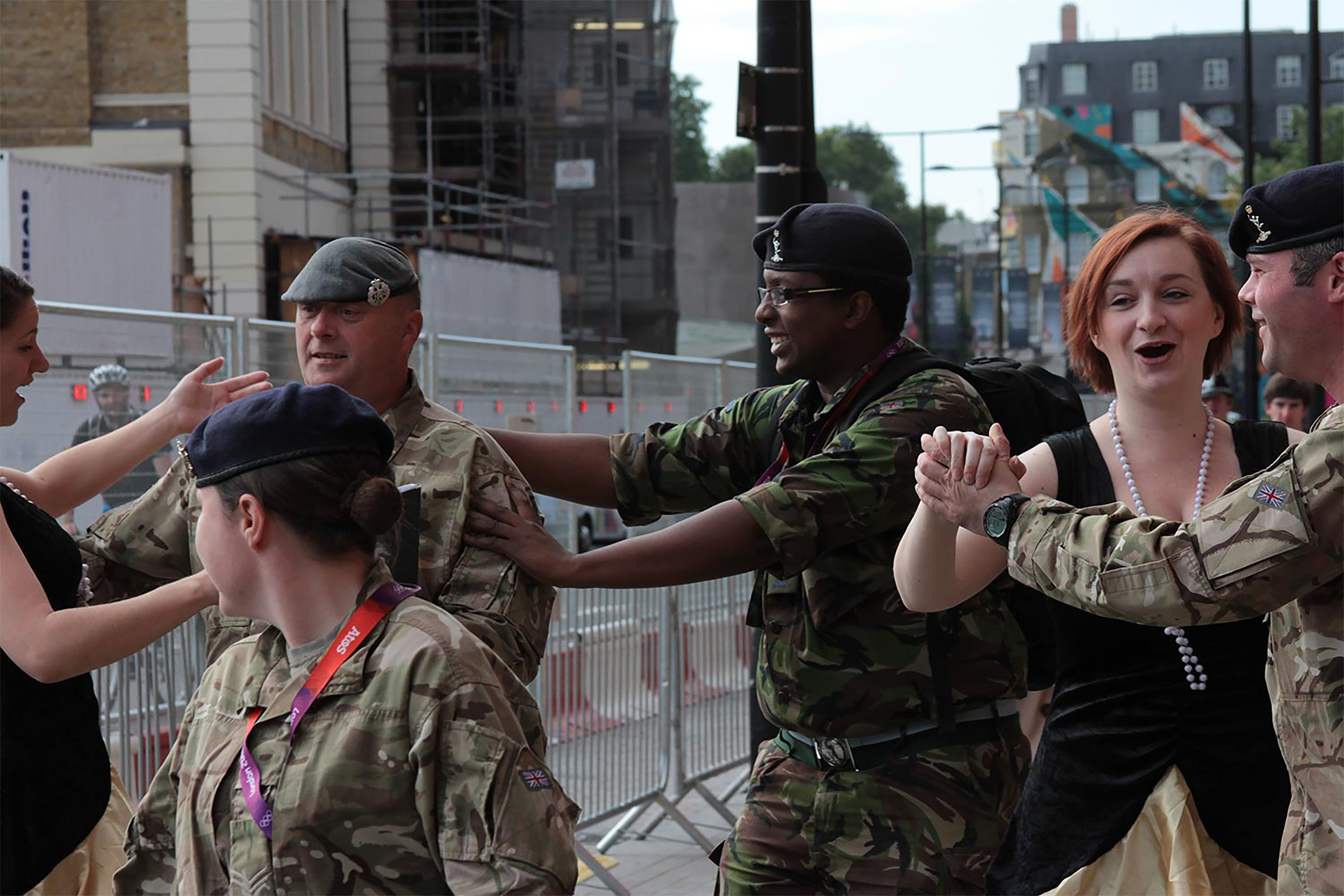 A group of dancers and army soldiers walking consecutively down the street.