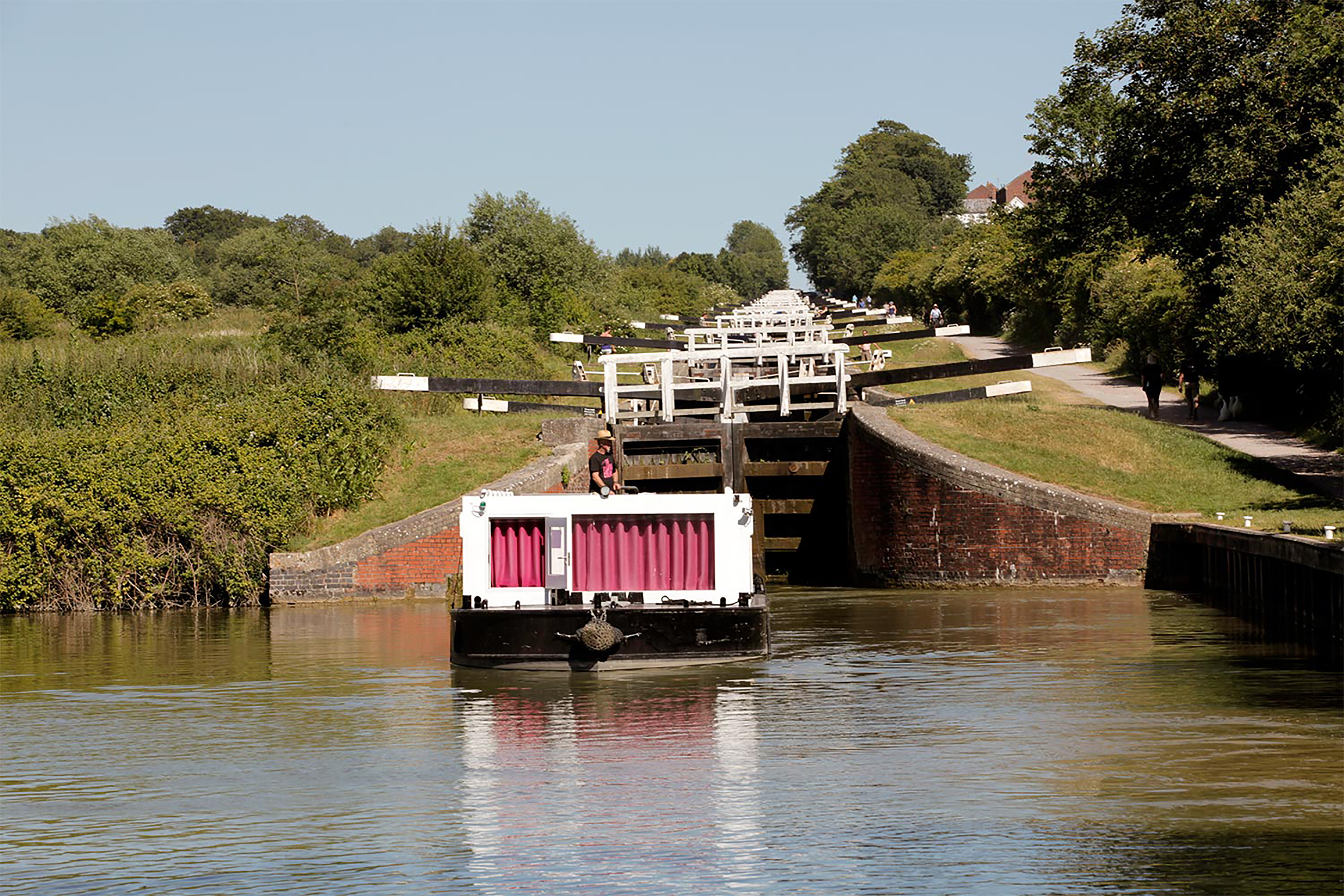 A large white canal boat on a river, next to a large lock.