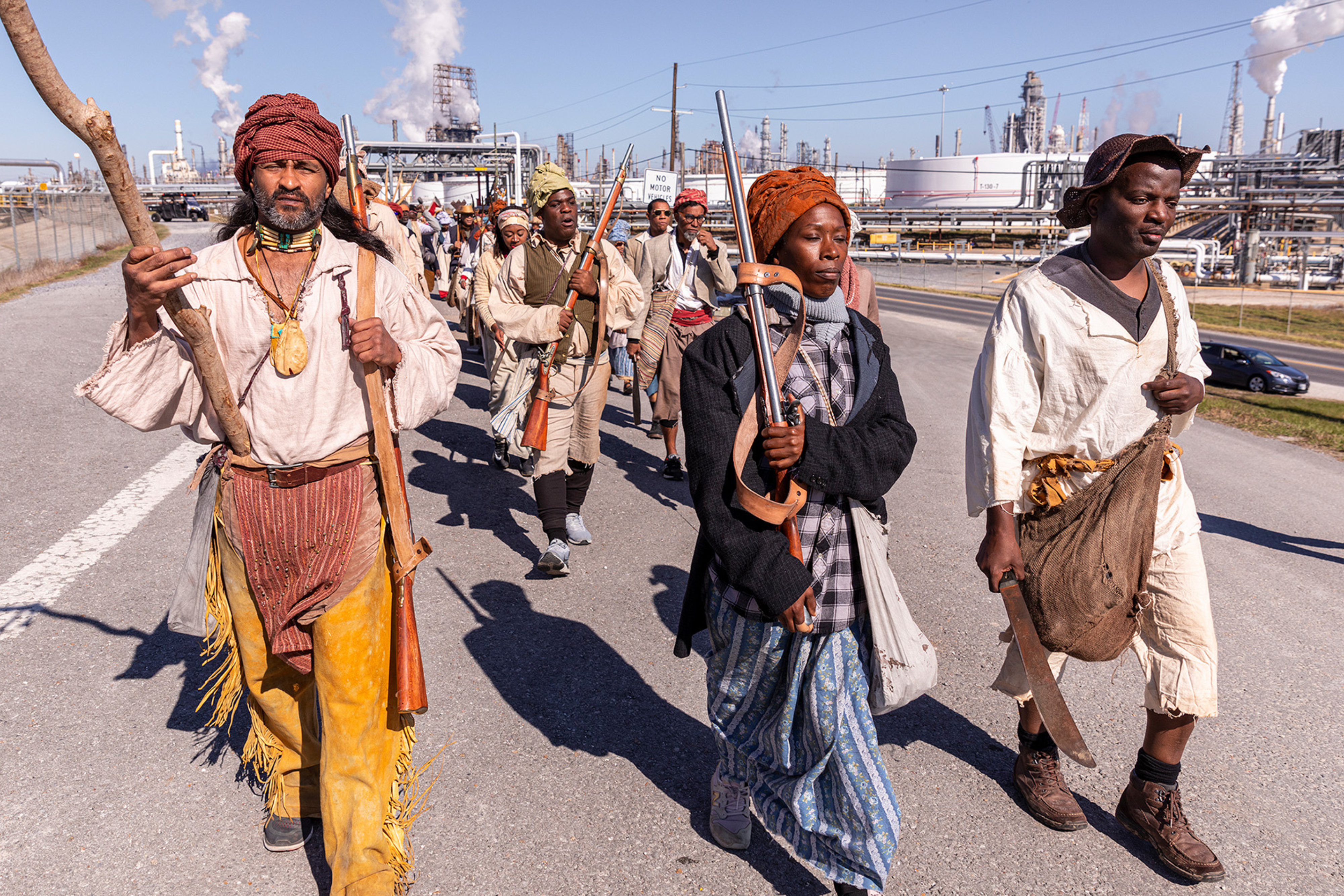 A group as people dressed as slaves carrying weapons walking up a highway.