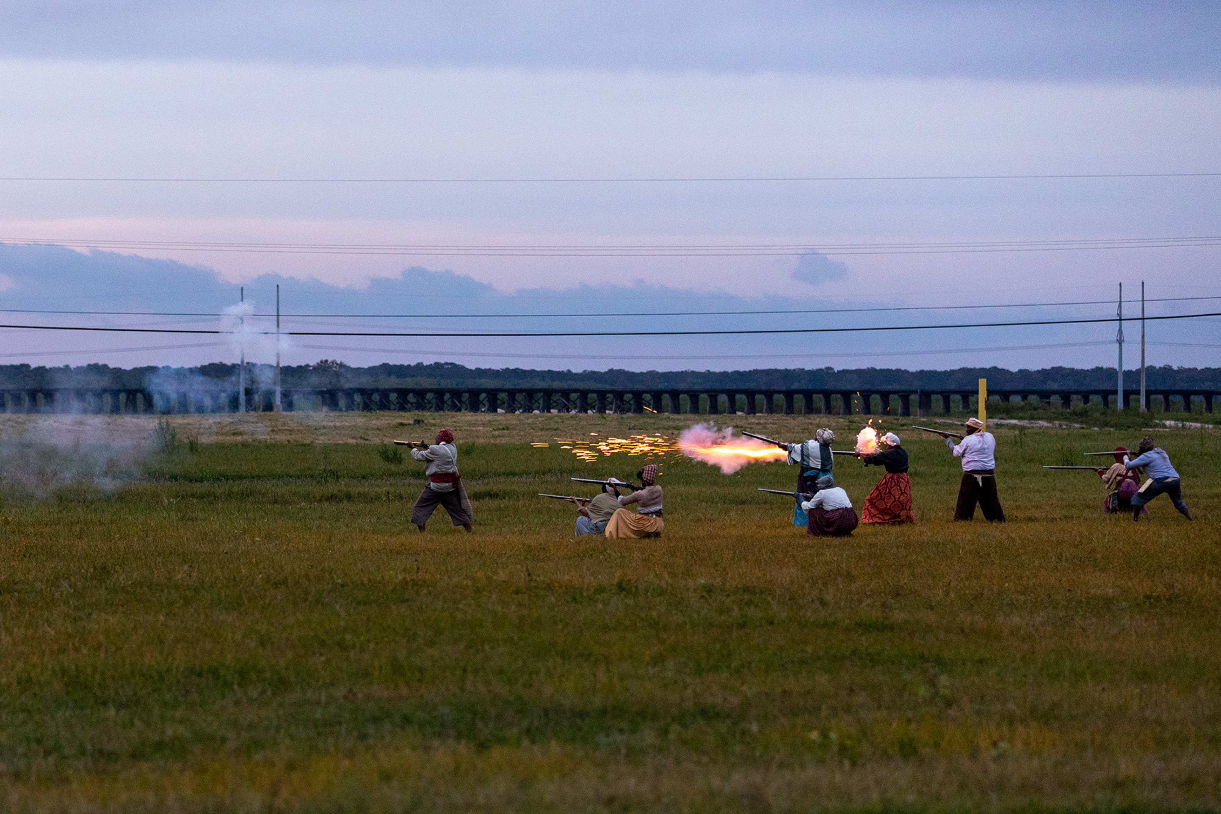 A group of people in a filed shooting various sizes of guns.