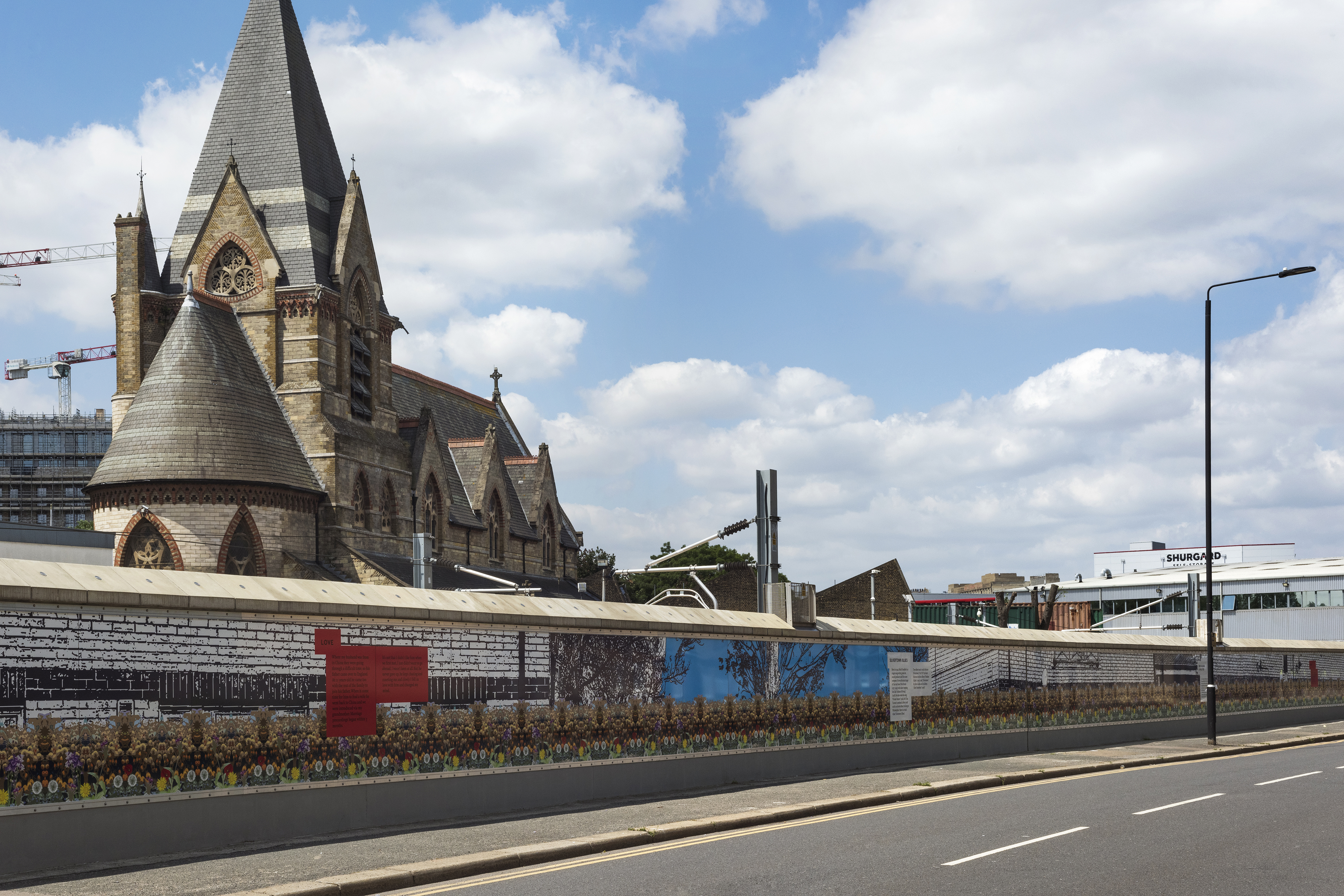A photograph of an empty road and a trackside wall covered in artistic murals in front of a Scottish Baronial Church.