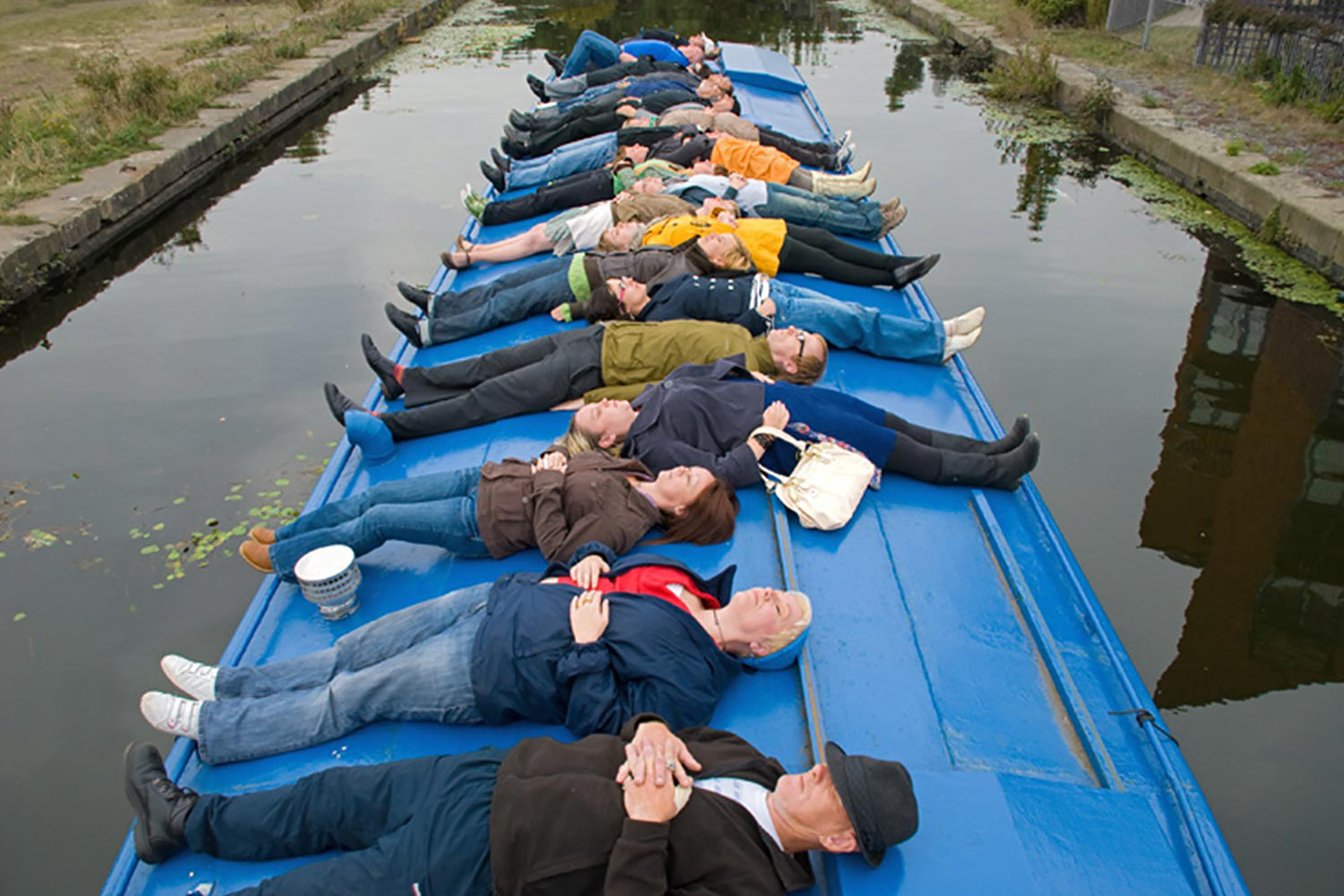 A photograph of a group of adults lying horizontally along a blue barge.