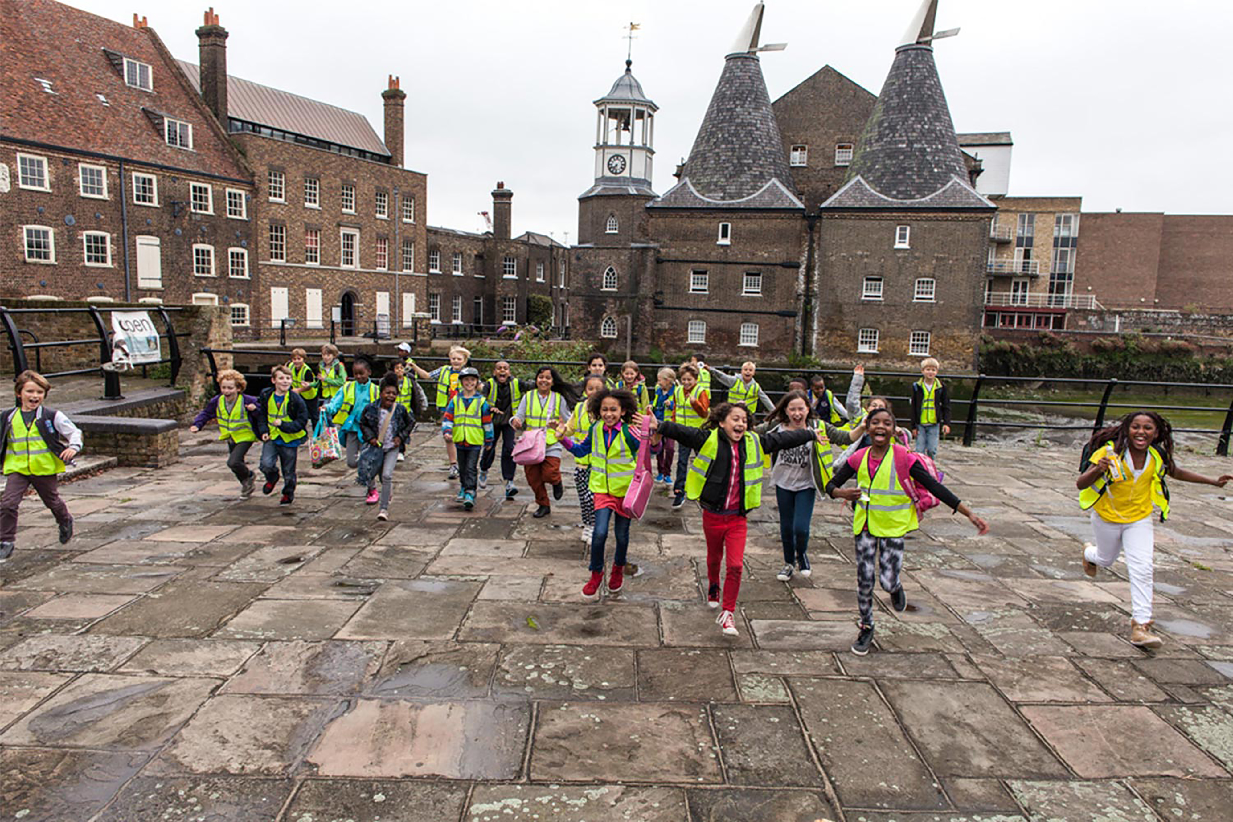 A crowd of children wearing green Hi-Vis jackets running across a courtyard surrounded by Scottish baronial architecture.