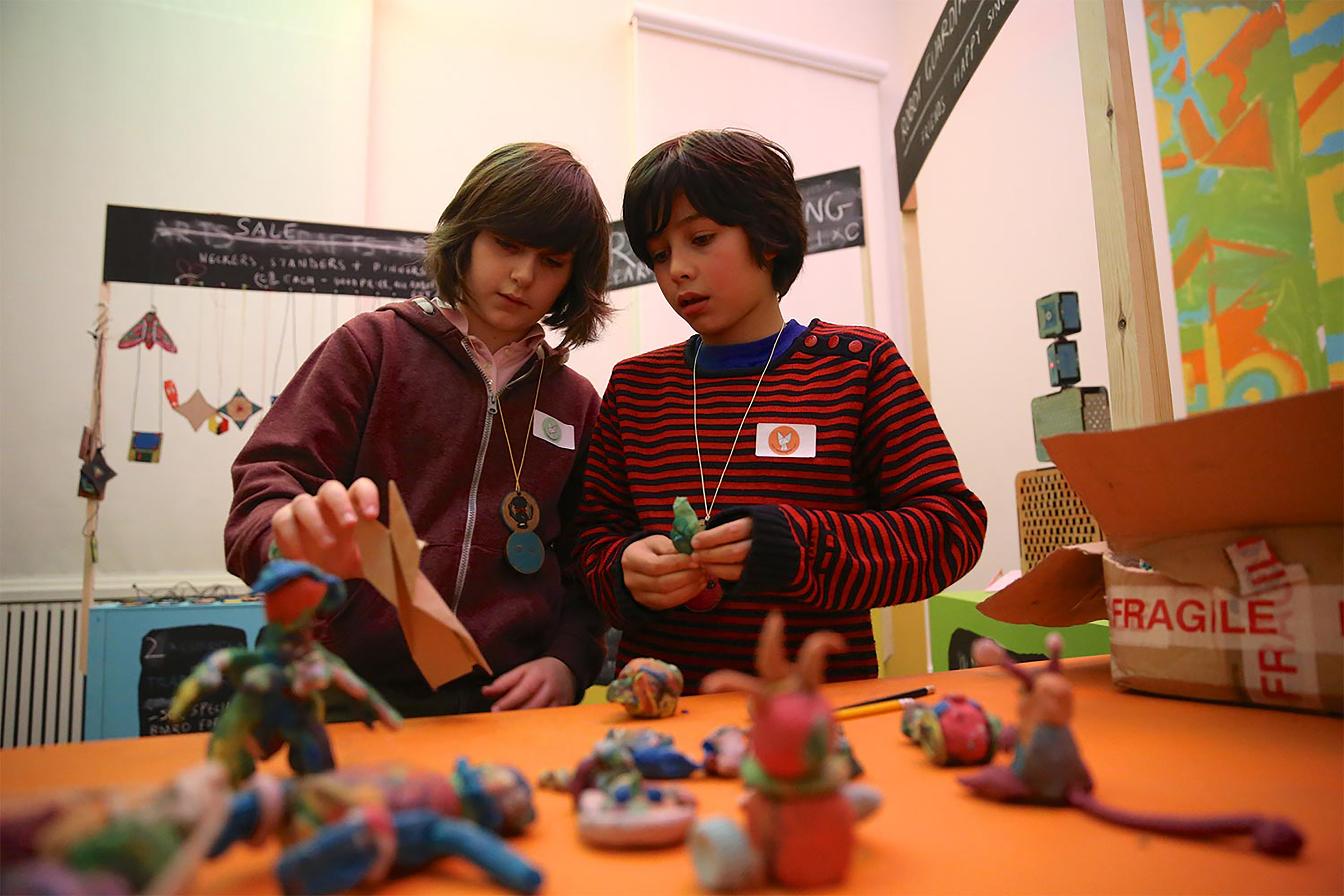 Two boys playing with origami and plasticine models on an orange table.