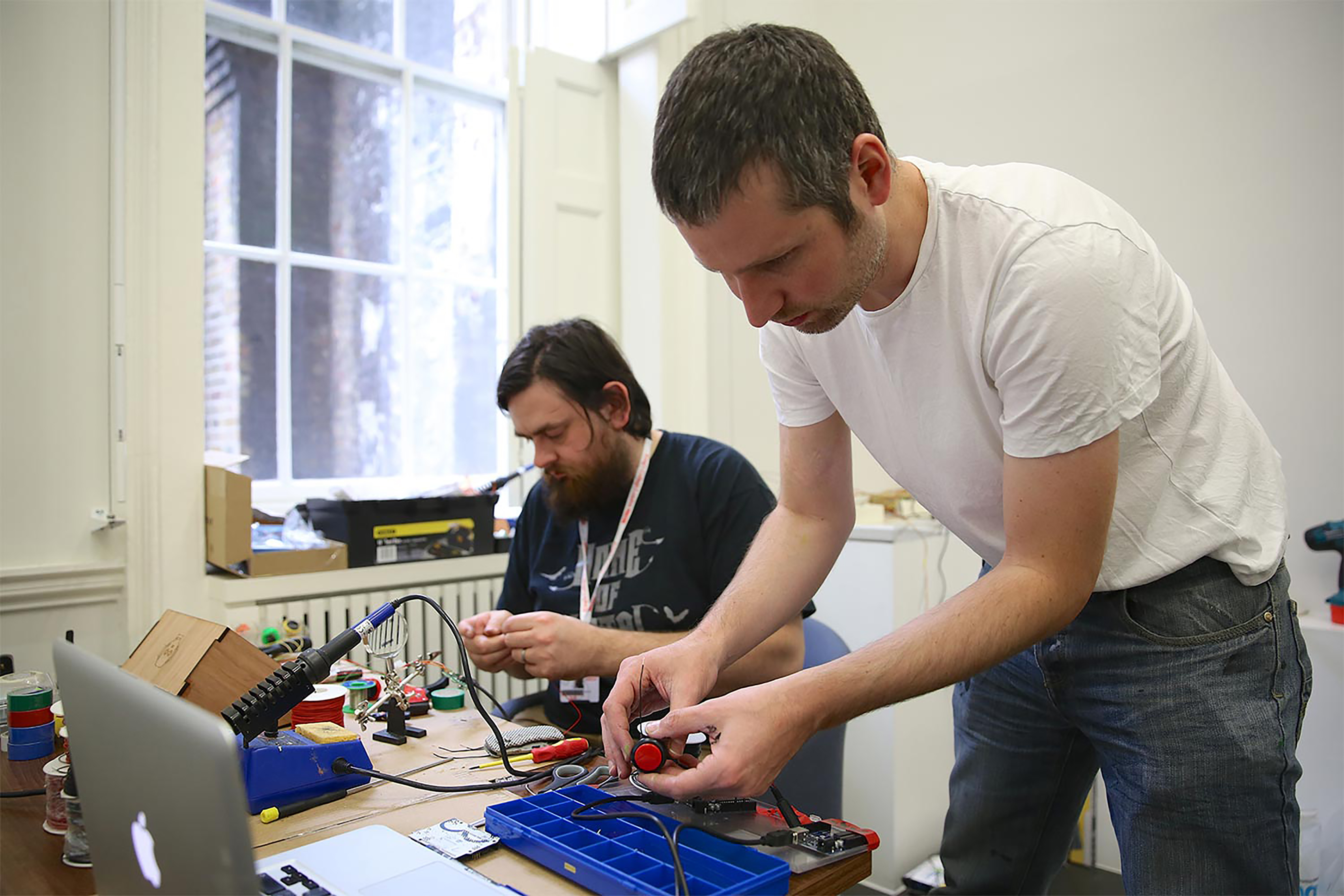 Two men wearing T-shirts inspecting electrical tools and cables in a studio.