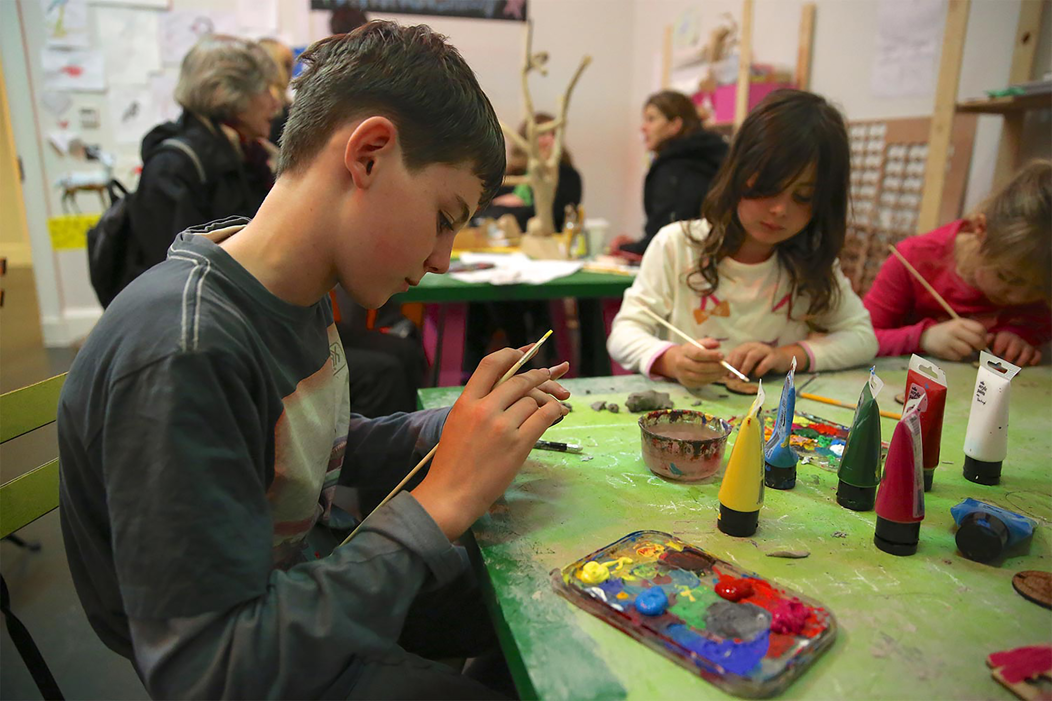 A photograph of a boy and a girl sitting at a green table using paint in a classroom.