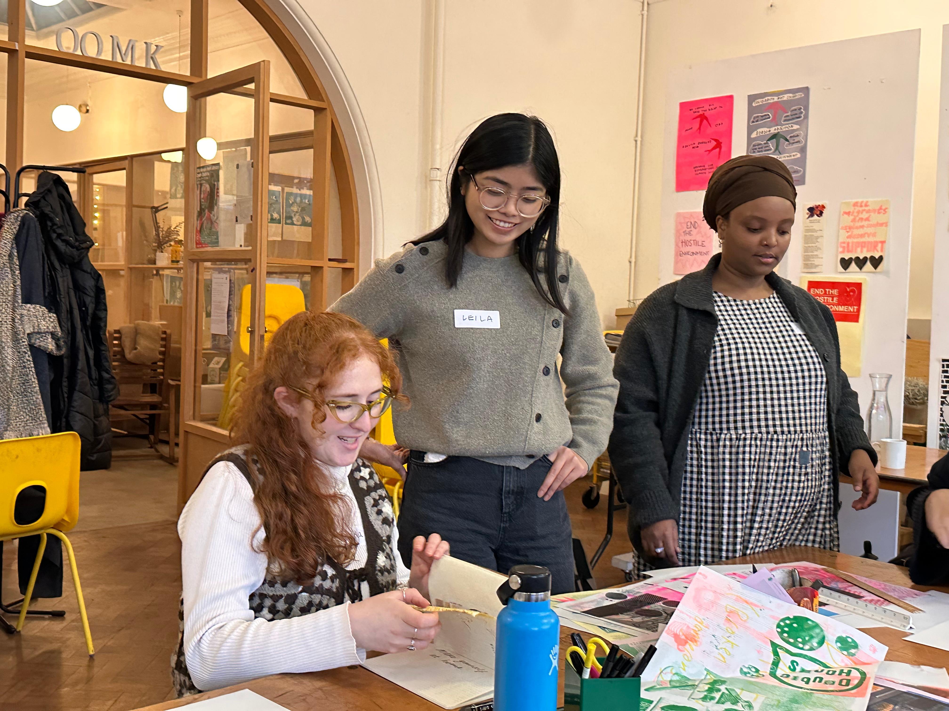 Three women around a table taking part in collaging and print activities in discussion with eachother