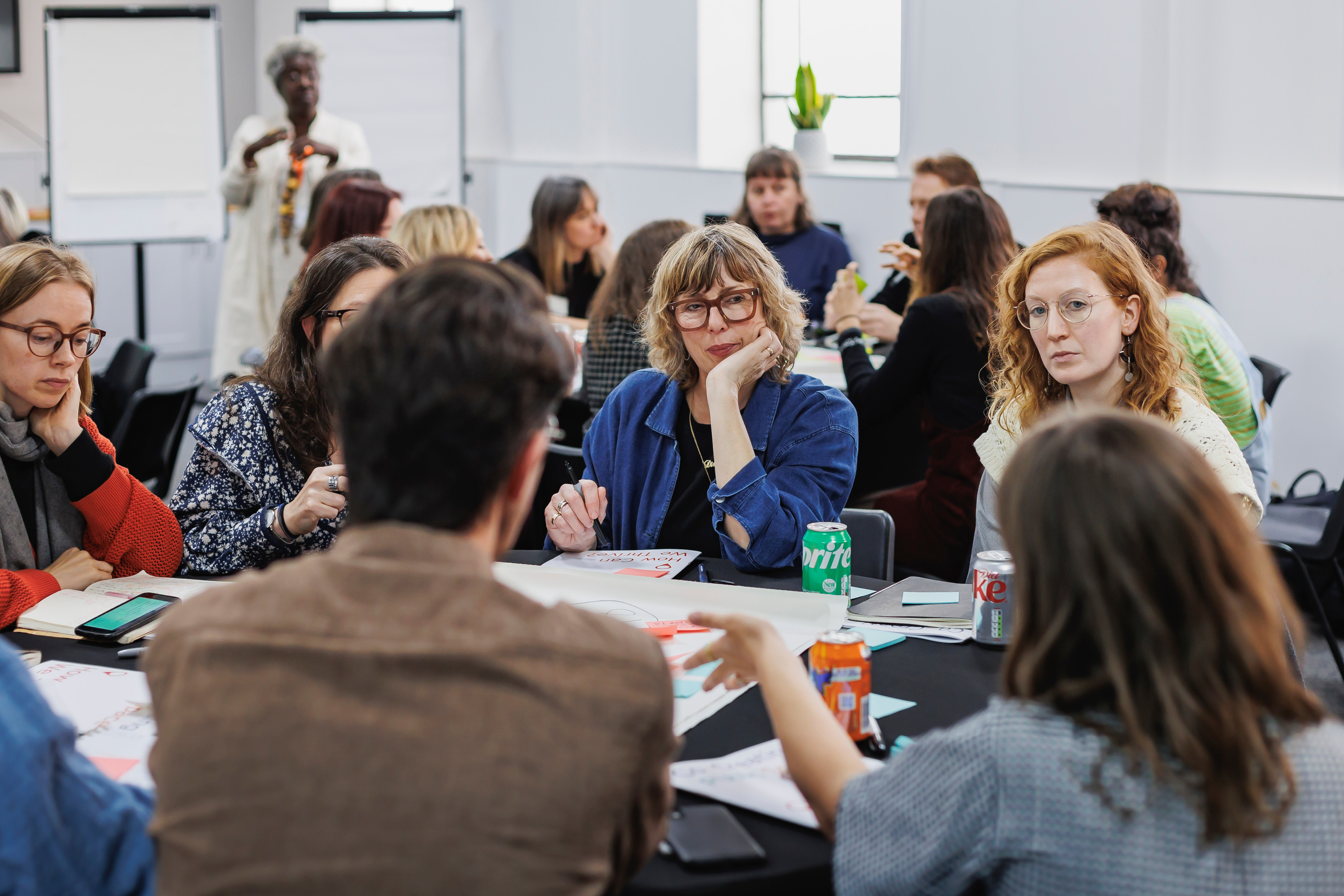 A group of people sitting round a table facing each other. They are speaking and the table contains various materials, pens and paper.
