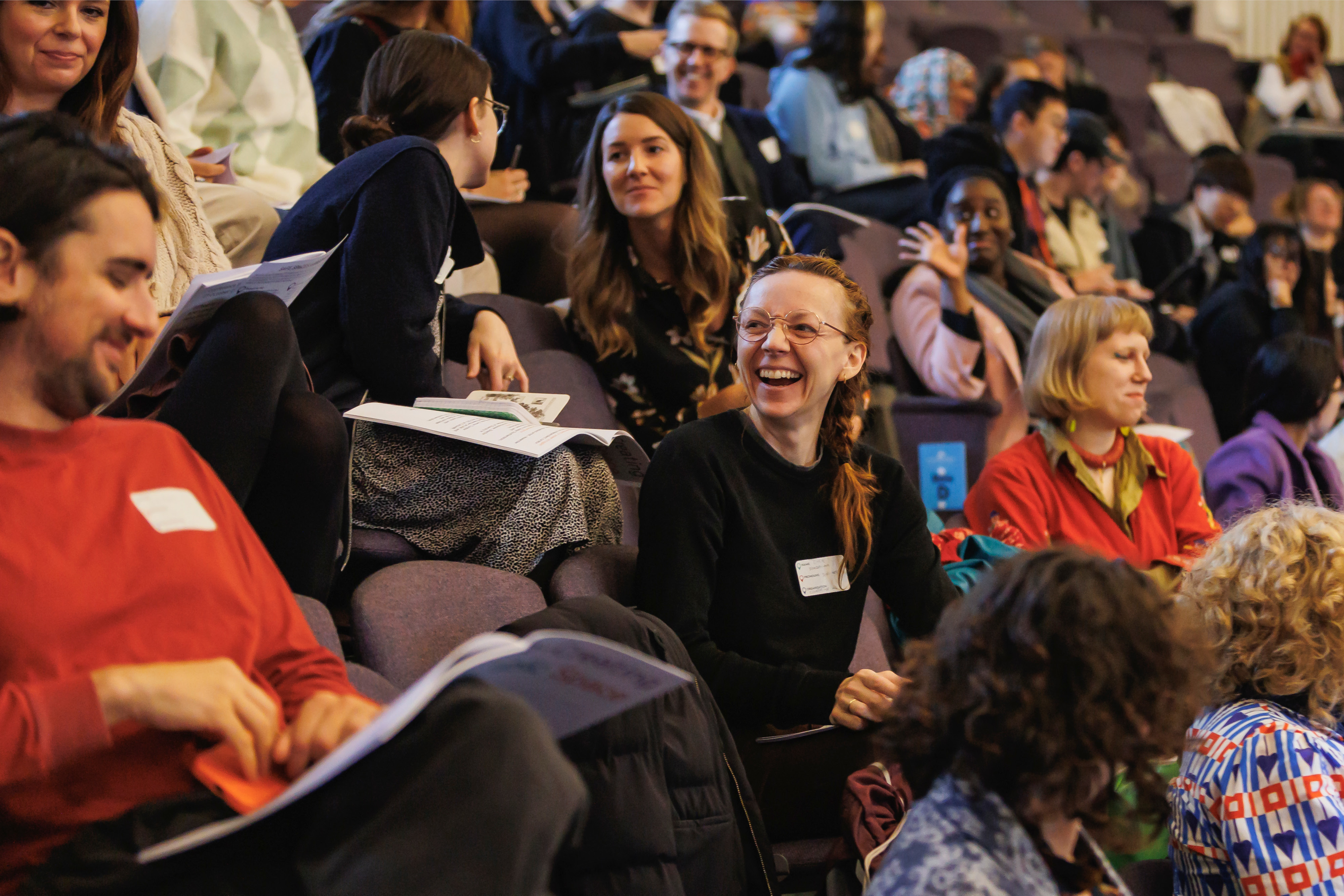 A group of people sitting in rows in an auditorium all talking and smiling.