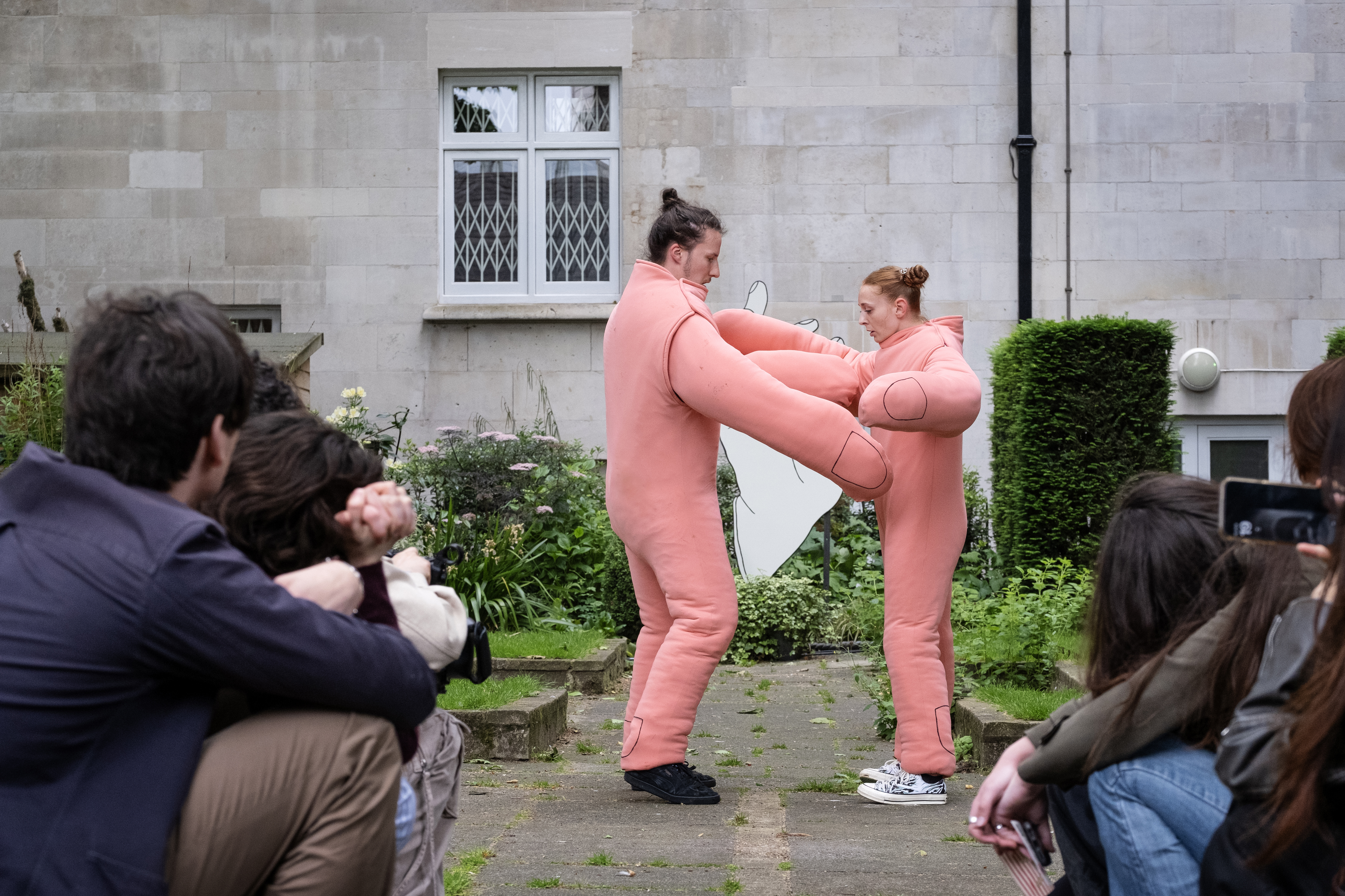 Two dancers dressed as hands dance in a church courtyard surrounded by an audience.