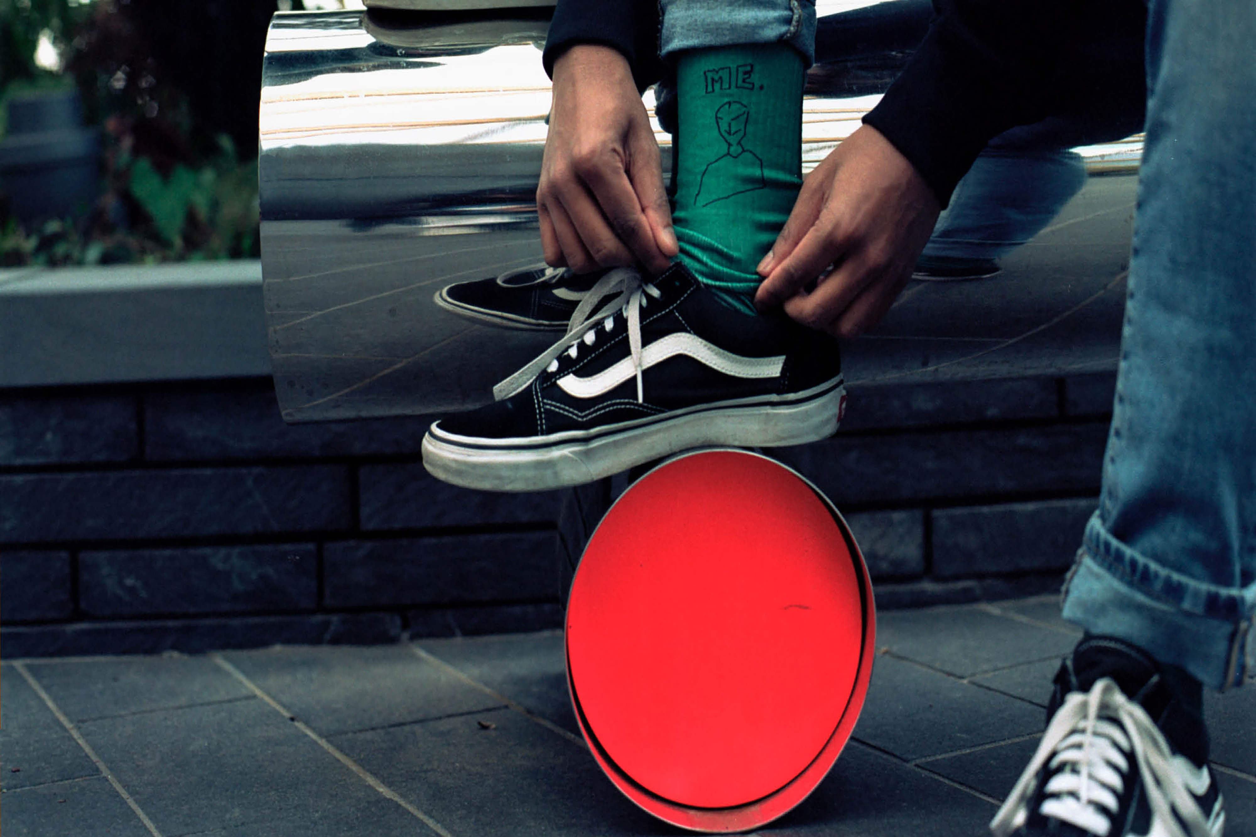 A person tying their shoelaces while balancing their foot on an orange circular block, wearing green socks and blue jeans.