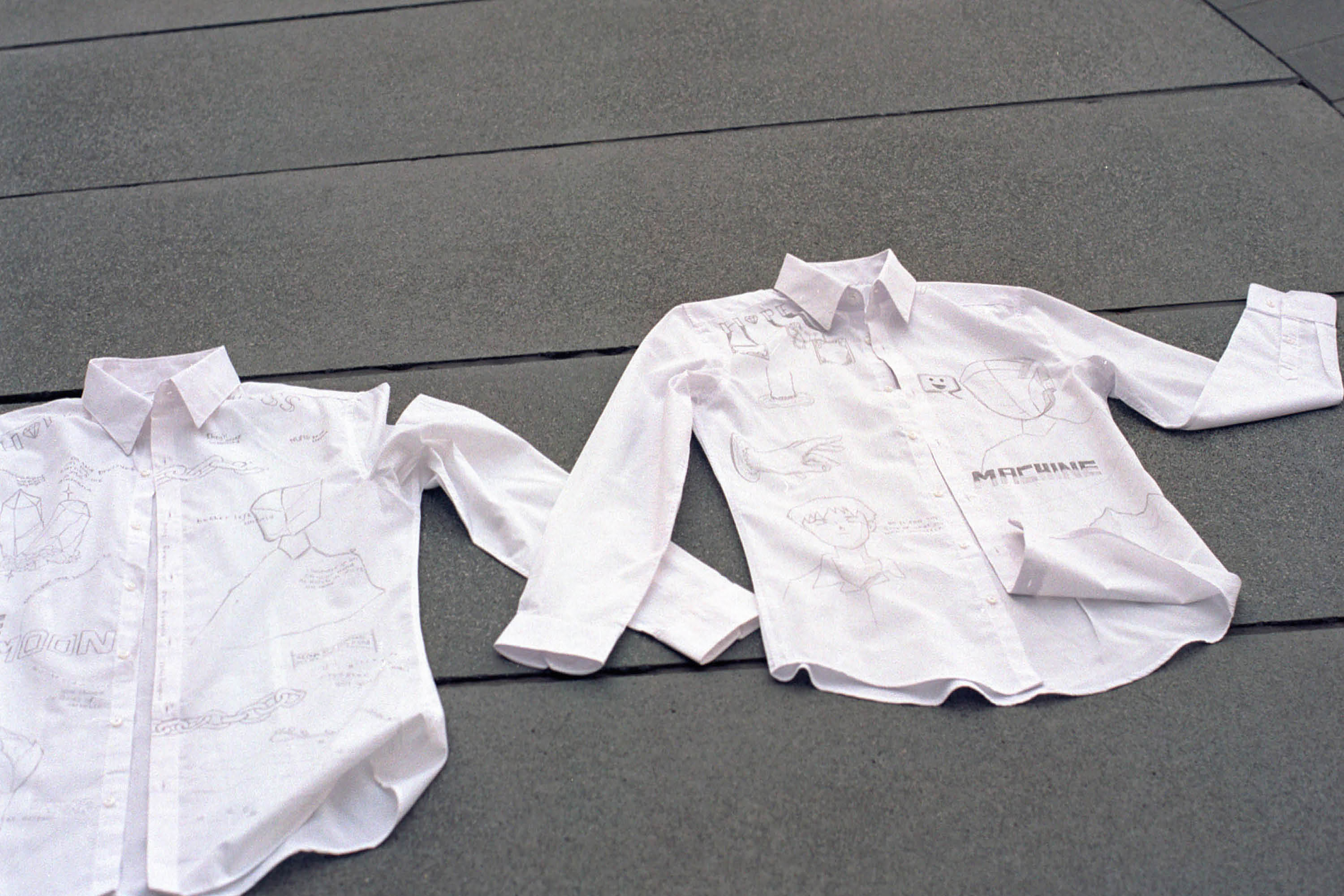 Two white shirts lying flat on a grey concrete floor next to each other.